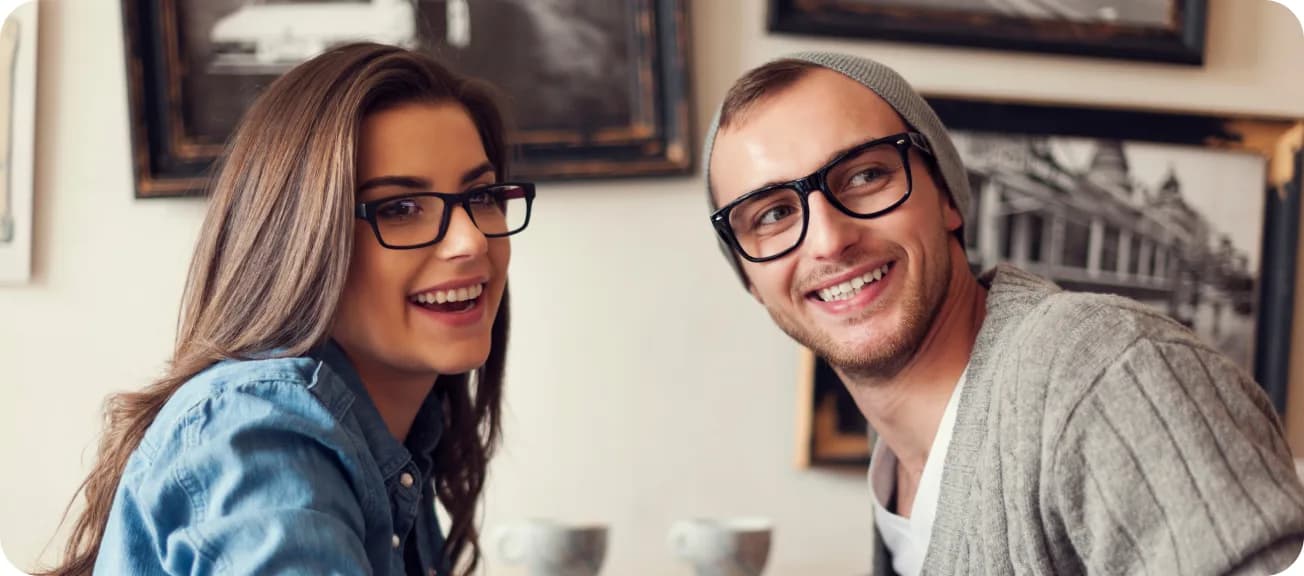 Un couple souriant portant des lunettes, attablé dans un café