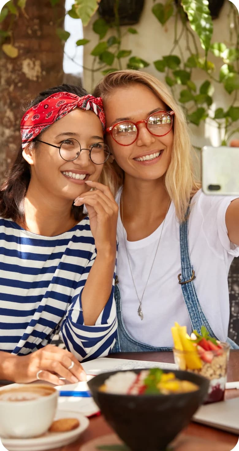 Deux amies souriantes prenant un selfie autour d'un petit-déjeuner