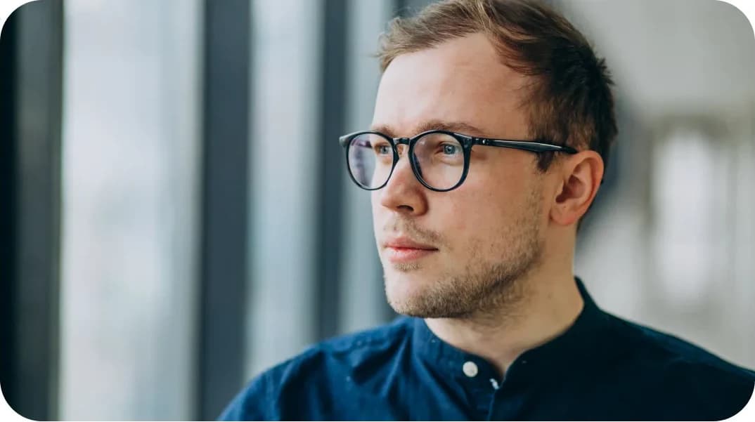 Un homme portant des lunettes, le regard tourné vers une fenêtre